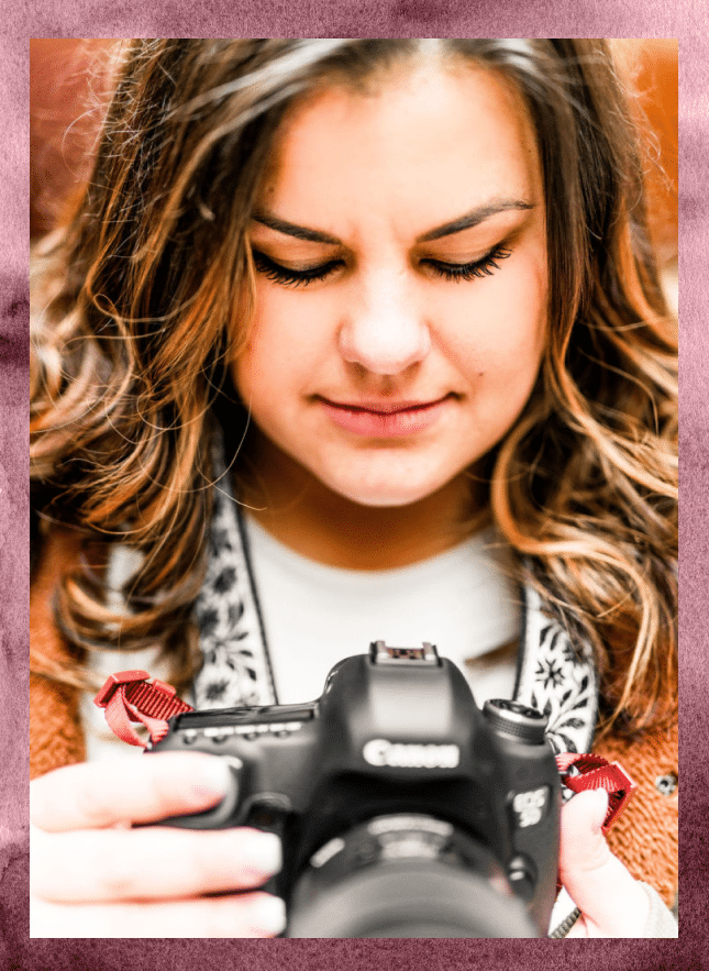 Andrea smiling holding her camera, smiling with a Pink Watercolor background